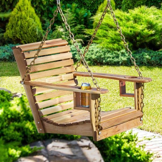 A wooden swing chair in the middle of a garden.