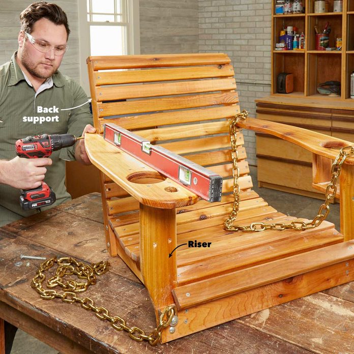 A man holding a drill next to a wooden chair.