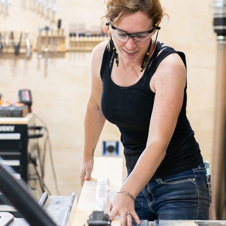 A woman in glasses is cutting paper with a knife.