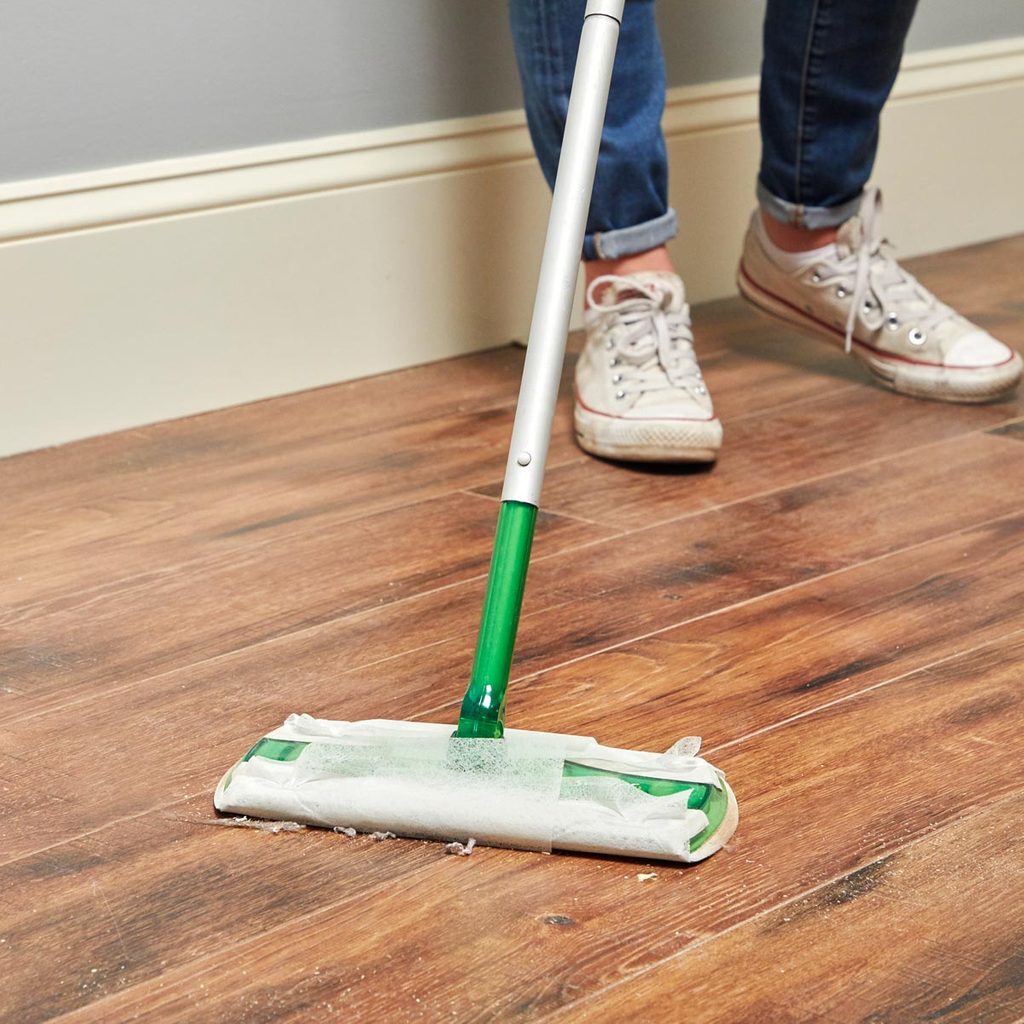 A person with white shoes and green mop on the floor.