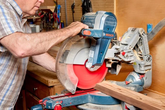 A man using a miter saw on wood.