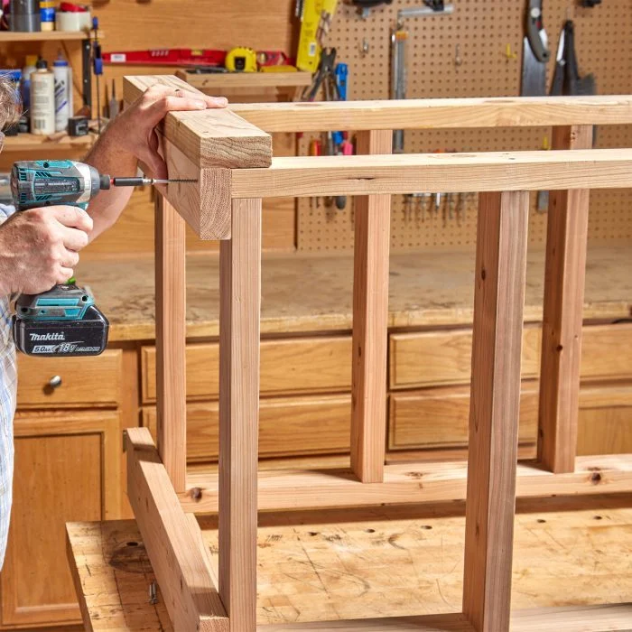 A person holding a drill in front of a wooden frame.