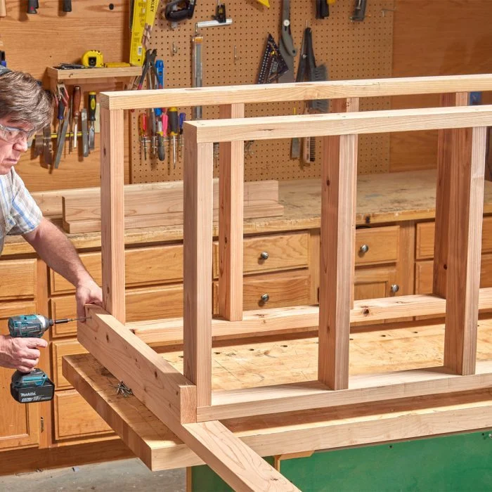 A man holding a drill in front of a wooden structure.