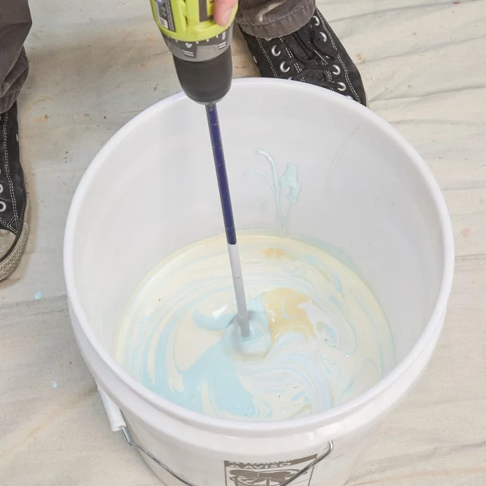 A person using a drill to paint the inside of a bucket.