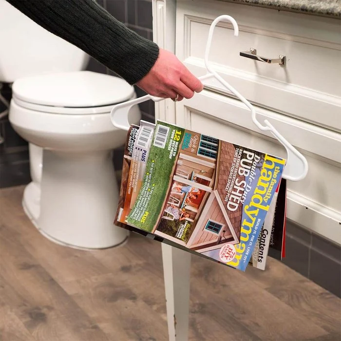 A person holding onto a magazine rack in front of the toilet.