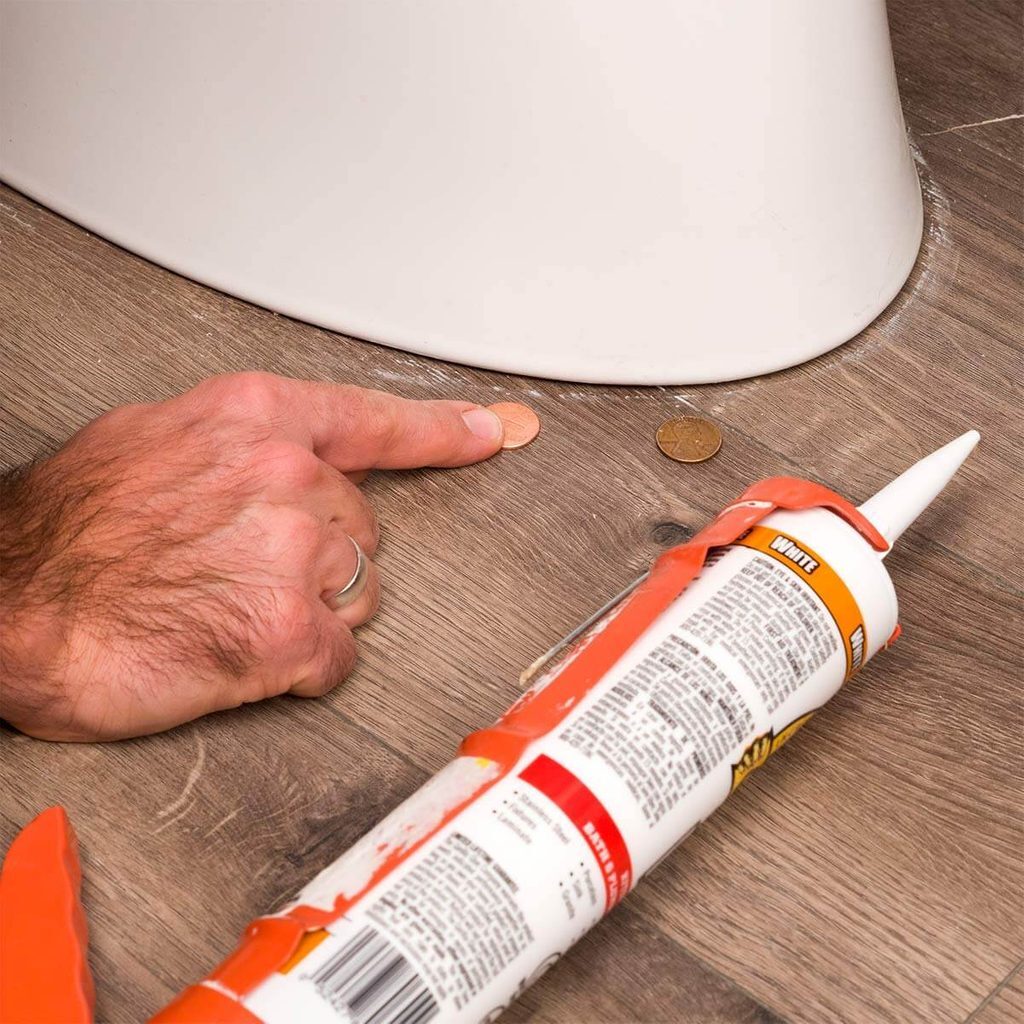 A person with their hand on the floor and a tube of glue