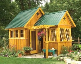 A yellow and green shed with flowers in the grass.