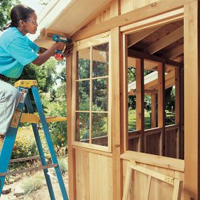 A woman standing on the ladder and using a drill to work on a window.